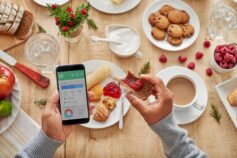 Person eating jam on toast while using a calorie tracker app to monitor their food intake.