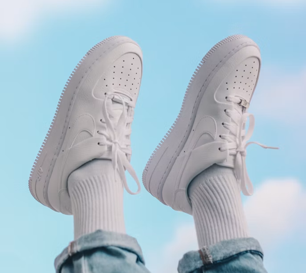White sneakers with white socks and blue jeans against a blue sky.