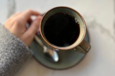 “A cup of black coffee on a table, held by a woman