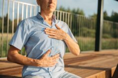 Middle-aged man sitting outdoors with one hand on his chest and the other on his stomach.