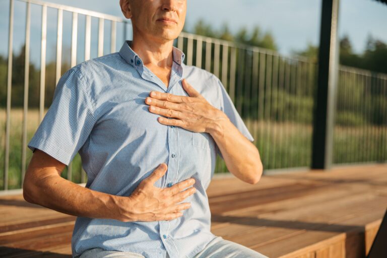 Middle-aged man sitting outdoors with one hand on his chest and the other on his stomach.