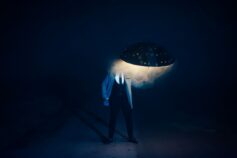 Person standing under a glowing umbrella in the dark.