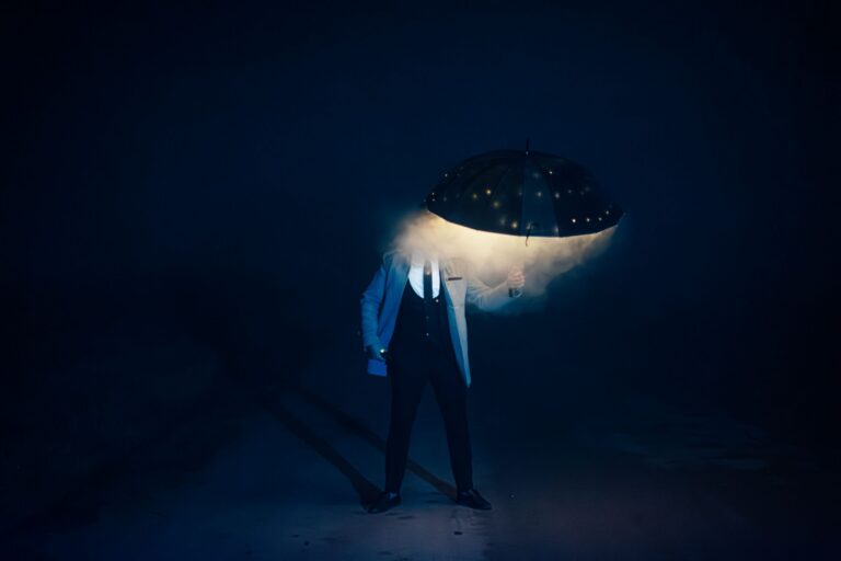 Person standing under a glowing umbrella in the dark.