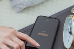 Hand turning off a smartphone alarm beside a bedside clock